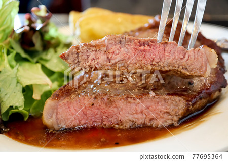Close-up piece sliced in the fork of sirloin beef steak with brown sauce in white plate background. Medium level ripe. Foods concept. 77695364