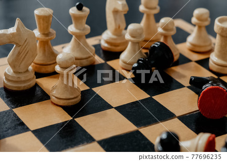 Old chess board with set of black and white pieces standing in chaotic position with some pieces laying on board Old chess board with set of black and white pieces standing in chaotic position with some pieces laying on board 77696235