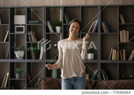 Joyful female teenager in headphones move in dance at home 77696964