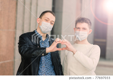 Young gay couple wearing medical mask, hugging and kissing at the city. Young gay couple wearing medical mask, hugging and kissing at the city. 77697033