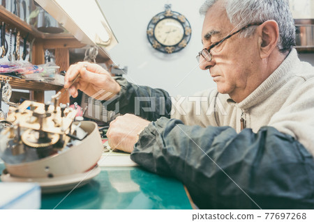 Watchmaker in his workshop repairing a larger clock 77697268