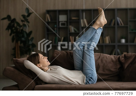 Casual young female relax barefoot on couch raise legs up 77697729