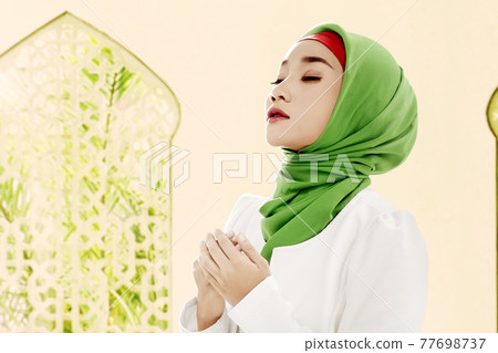 Asian Muslim woman in a veil standing while raised hands and praying 77698737