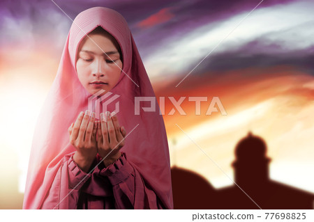 Asian Muslim woman in a veil standing while raised hands and praying Asian Muslim woman in a veil standing while raised hands and praying 77698825