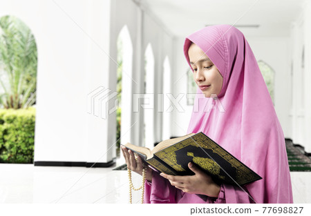 Asian Muslim woman in a veil holding prayer beads and reading the Quran Asian Muslim woman in a veil holding prayer beads and reading the Quran 77698827