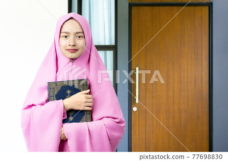 Asian Muslim woman in a veil standing and holding the Quran Asian Muslim woman in a veil standing and holding the Quran 77698830