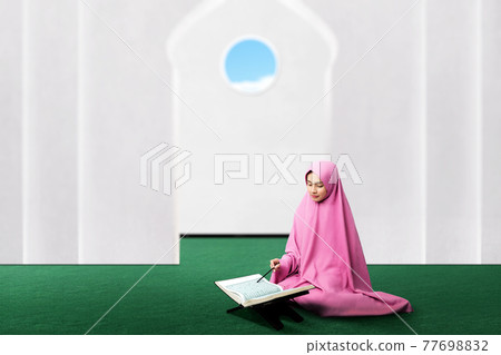 Asian Muslim woman in a veil sitting and reading the Quran Asian Muslim woman in a veil sitting and reading the Quran 77698832