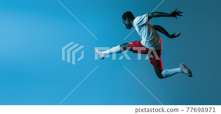 African soccer football player jumping isolated on blue background in neon light. Flyer African soccer football player jumping isolated on blue background in neon light. Flyer 77698971