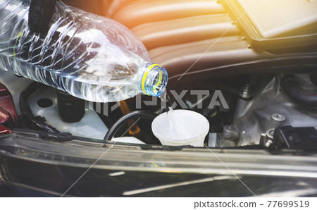 Mechanic hand was pouring clean water into the water reserve tank of the car engine Mechanic hand was pouring clean water into the water reserve tank of the car engine 77699519