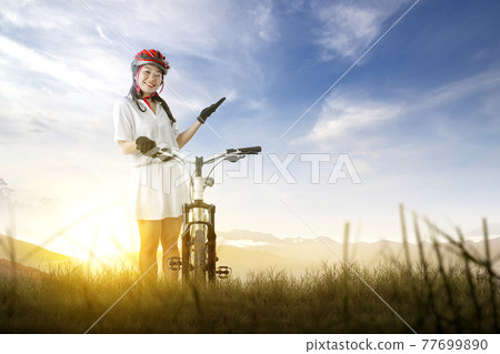 Asian woman with a bicycle helmet standing beside her bicycle 77699890