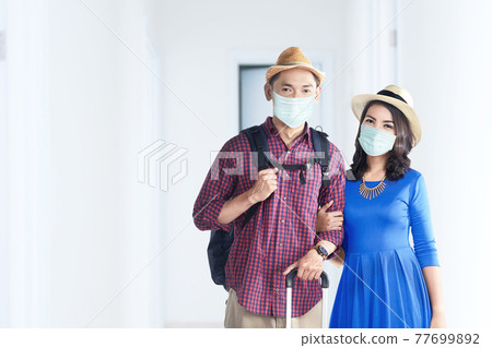 Asian couple in the face mask with suitcase bag and backpack on the hospital Asian couple in the face mask with suitcase bag and backpack on the hospital 77699892