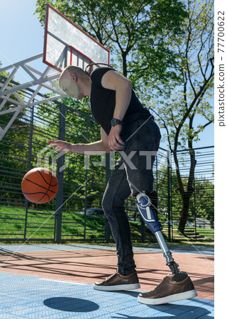 athletic young man with artificial leg practice basketball on a cort 77700622