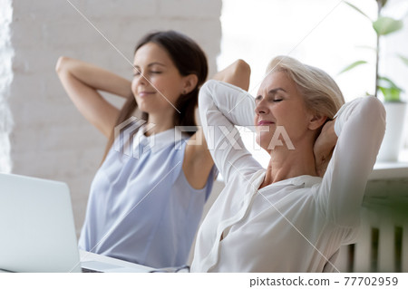 Calm female colleagues relax sitting at office desk 77702959