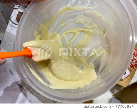 Melted hot white yummy sweet little round chocolate callets made from Belgian milk chocolate for tempering and making homemade sweet desserts and garnishes 77703854
