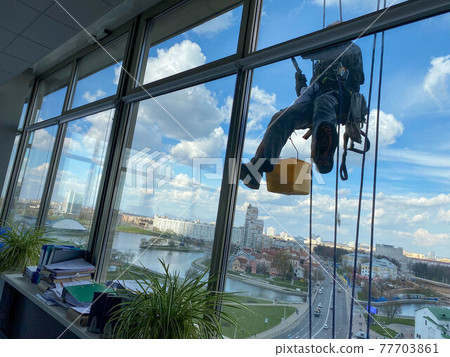 Professional industrial climber in rubber gloves washes windows at high altitude Professional industrial climber in rubber gloves washes windows at high altitude 77703861