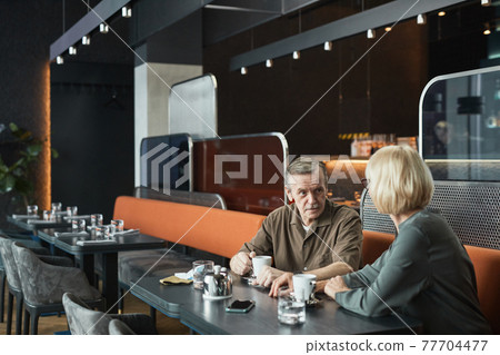 Senior man with tea cup chatting with woman Senior man with tea cup chatting with woman 77704477
