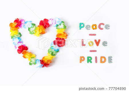 Hawaiian flower necklace in the shape of a heart with Peace Love Pride inscription on the white background. LGBTQ concept with rainbow flag colors. Pride month. Selective focus. Copy space. 77704890