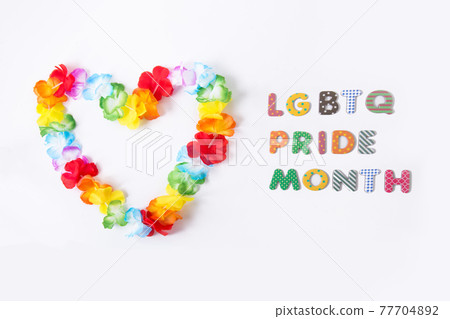 Hawaiian flower necklace in the shape of a heart with LGBTQ Pride month inscription on the white background. LGBT concept with rainbow flag colors. Selective focus. Copy space 77704892