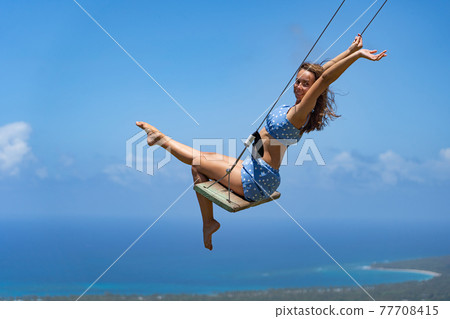 Young beautiful caucasian woman on the rope swing with sea and sky background. Concept of joy and leisure  77708415