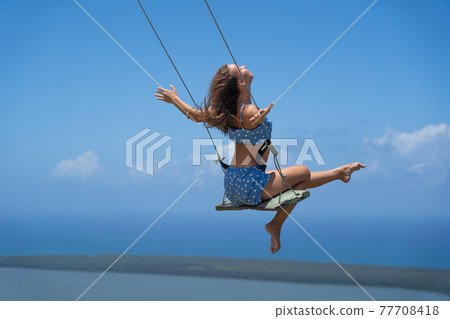 Young beautiful caucasian woman on the rope swing with sea and sky background. Concept of Vacation and travel  77708418