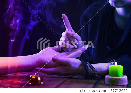 Witch is a fortune teller reading good luck close-up. Fortune teller guides the lines on the client's hand in neon light 77712051
