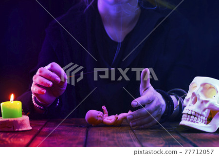 A fortune teller, witch or oracle performs a ritual on a baby doll. Psychic readings and the concept of clairvoyance. Photo with neon light A fortune teller, witch or oracle performs a ritual on a baby doll. Psychic readings and the concept of clairvoyance. Photo with neon light 77712057
