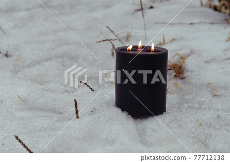 Grunge black candle burning outside in winter. Esoteric, gothic and occult background, Halloween mystic and wicca concept outdoors. 77712138