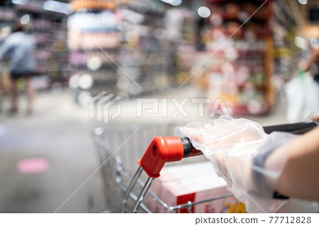 People wearing plastic glove pushing a shopping cart,prevention spread infection of COVID-19,Coronavirus,plastic gloves service from the supermarket before shop,concept of safety,hygiene,health care 77712828