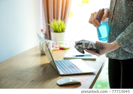 Business woman work from home wearing protection mark in covid-19 virus situation. Her working in quarantine for coronavirus and cleaning her laptop with sanitizer or alcohol gel. 77713045