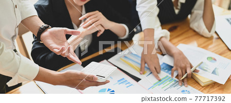 Business people are meeting together at the wooden working desk surrounded by paperwork. Business people are meeting together at the wooden working desk surrounded by paperwork. 77717392