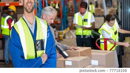 Mid section of happy caucasian worker wearing yellow vest in an warehouse in front of hid colleagues 77718108