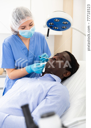 Female beautician injecting facial filler to male client in clinic Female beautician injecting facial filler to male client in clinic 77718523