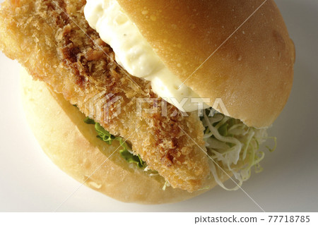A hamburger sandwiched between plenty of tartar sauce and fried white fish is photographed on a white background (overhead view) 77718785