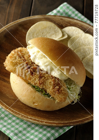 Plenty of tartar sauce, fried white fish sandwiches and potato chips on a wooden plate on a place mat 77719728