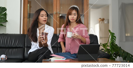 Asian women are sitting and relaxing together on the black leather sofa. 77723014