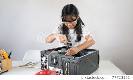A little girl is repairing computer hardware at the white working table. A little girl is repairing computer hardware at the white working table. 77723191