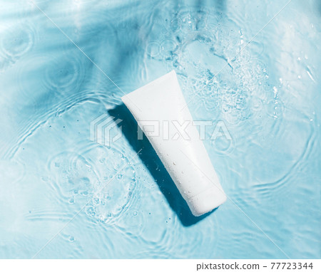 Cosmetic sunscreen product on blue water surface with splashes and drops. Body care health concept. Flat lay top view 77723344