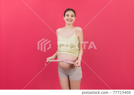 pregnant woman measuring her growing tummy with a tape measure at colored background. Check a baby development. Copy space 77723408