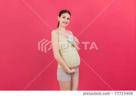 Happy pregnant woman holding baby girl booties against her belly at Colored background. Happy pregnancy. Copy space 77723409