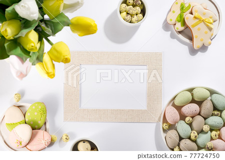 Easter table setting with a plate of colored pastel eggs, a bouquet of tulips and biscuits rabbits, photo frame for mockup 77724750