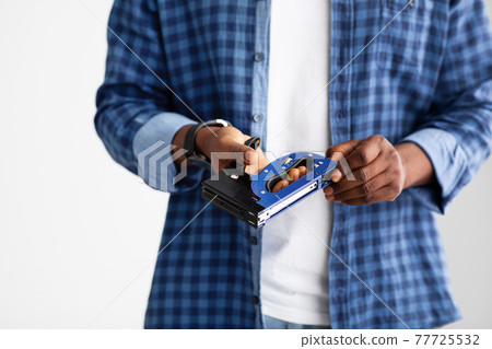 Unrecognizable black carpenter holding construction stapler in hands, standing over white background, crop Unrecognizable black carpenter holding construction stapler in hands, standing over white background, crop 77725532