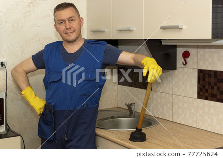 A satisfied plumber in kitchen by the sink with faucet with a plunger A satisfied plumber in kitchen by the sink with faucet with a plunger 77725624