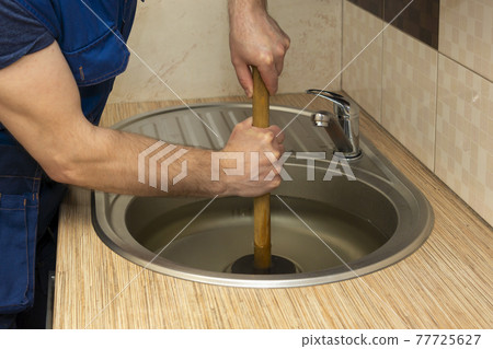 A plumber clear a blockage in a kitchen sink with a plunger 77725627