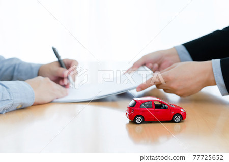 man signing a car insurance policy, the agent is holding the document. concept document sales loan and rental. focust red car on table 77725652