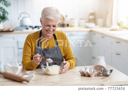 Joyful grandmother making dough at kitchen, copy space 77725658