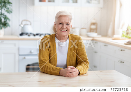 Smiling senior lady sitting at table in kitchen at home 77725718