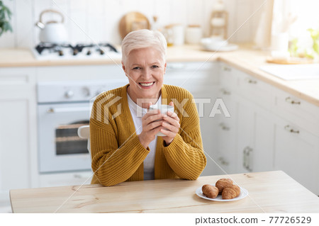 Cheerful elderly lady enjoying coffee with croissant 77726529
