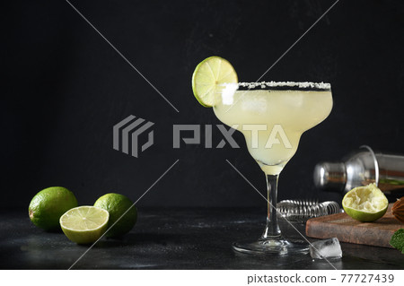 Classic Margarita cocktail with lime juice and ice cube on dark black background with copy space. 77727439