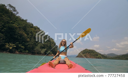 Sportive woman rows pink plastic canoe along sea water. Positive sports girl hand padding on kayak, front view. 77727458