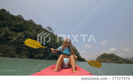 Sportive woman rows pink plastic canoe along sea water. Positive sports girl hand padding on kayak, front view. Sportive woman rows pink plastic canoe along sea water. Positive sports girl hand padding on kayak, front view. 77727470